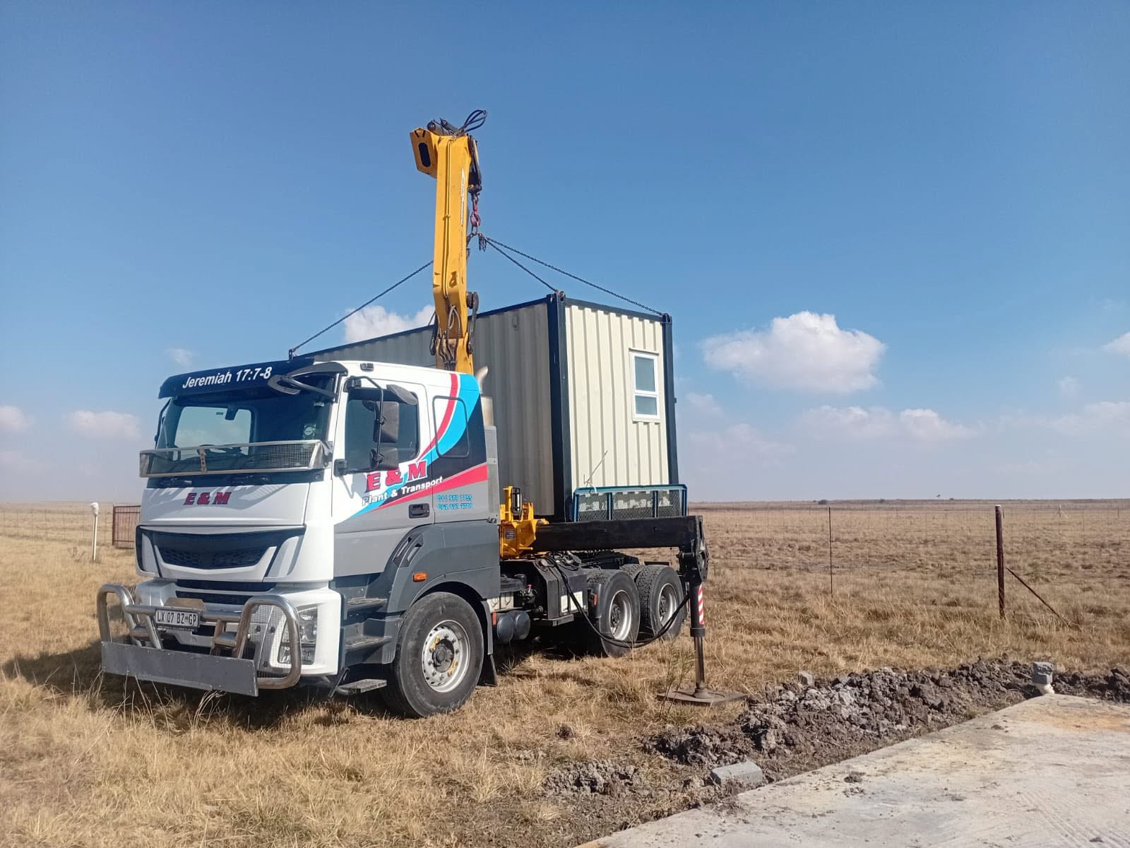 E&M crane truck lifting a portable office container on a rural South African site